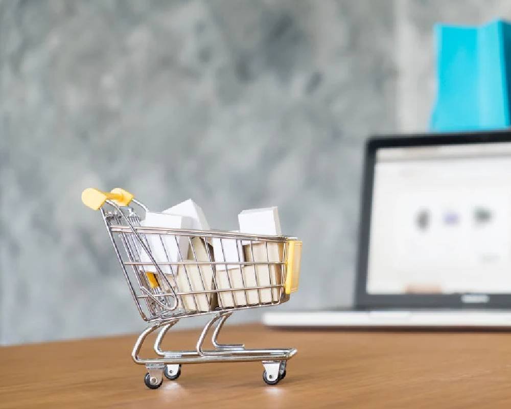 A mini shopping cart beside a laptop